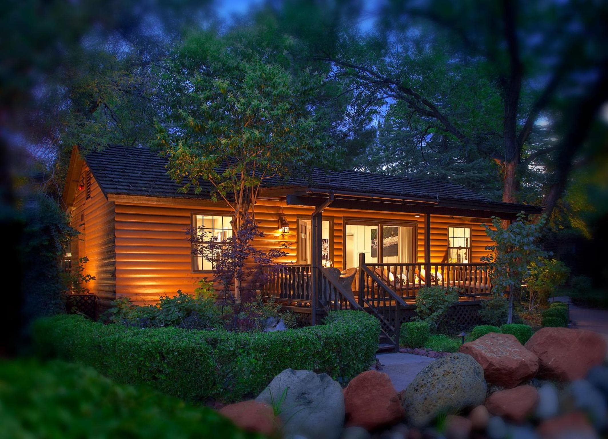 L'Auberge de Sedona cottage exterior glowing at dusk beneath the trees.